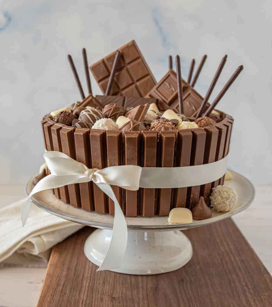 Side view of chocolate candy cake with a ribbon around it on a cake stand.