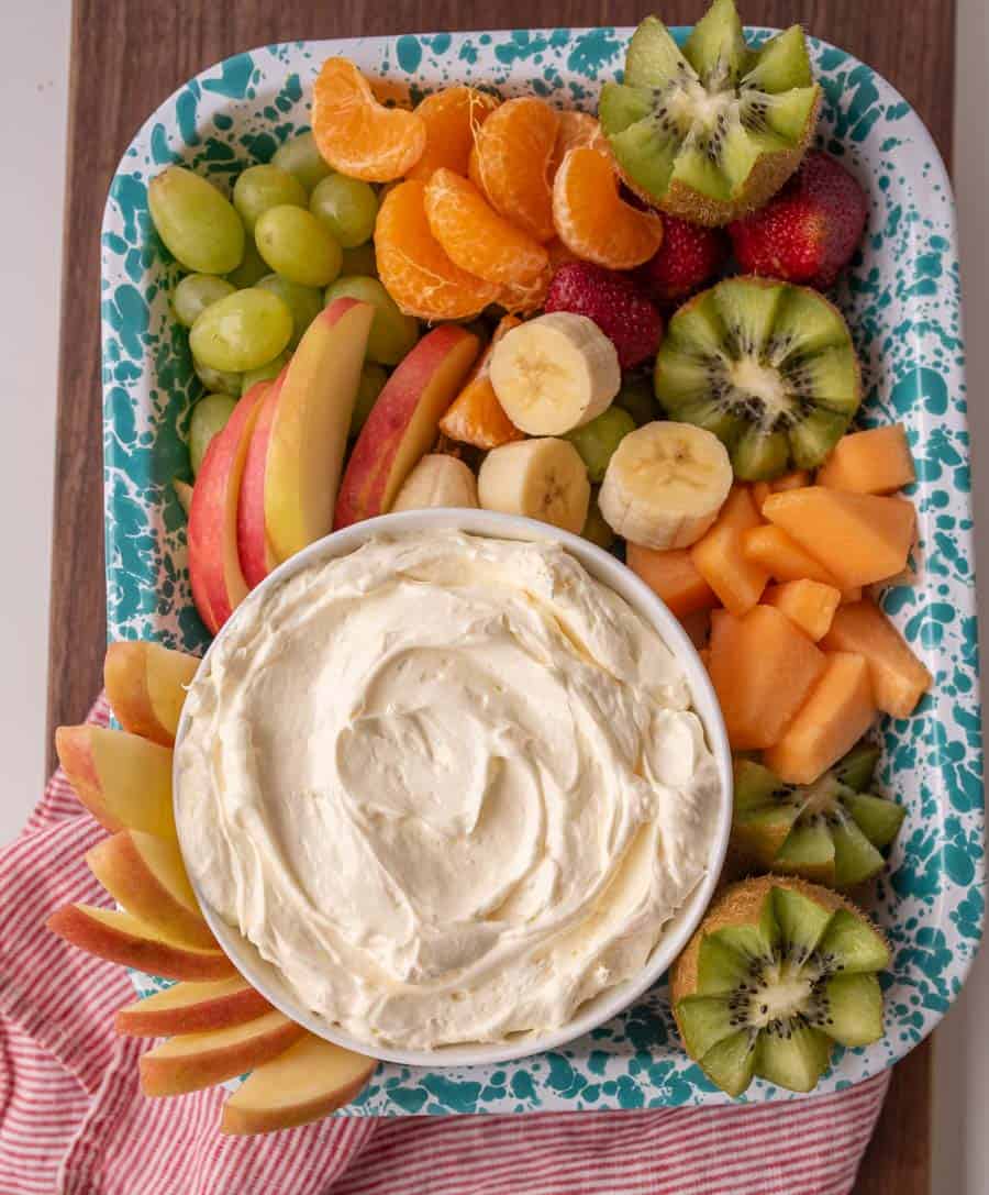 a bowl of fluffy fruit dip and slices of fruit on a blue speckled enamelware tray