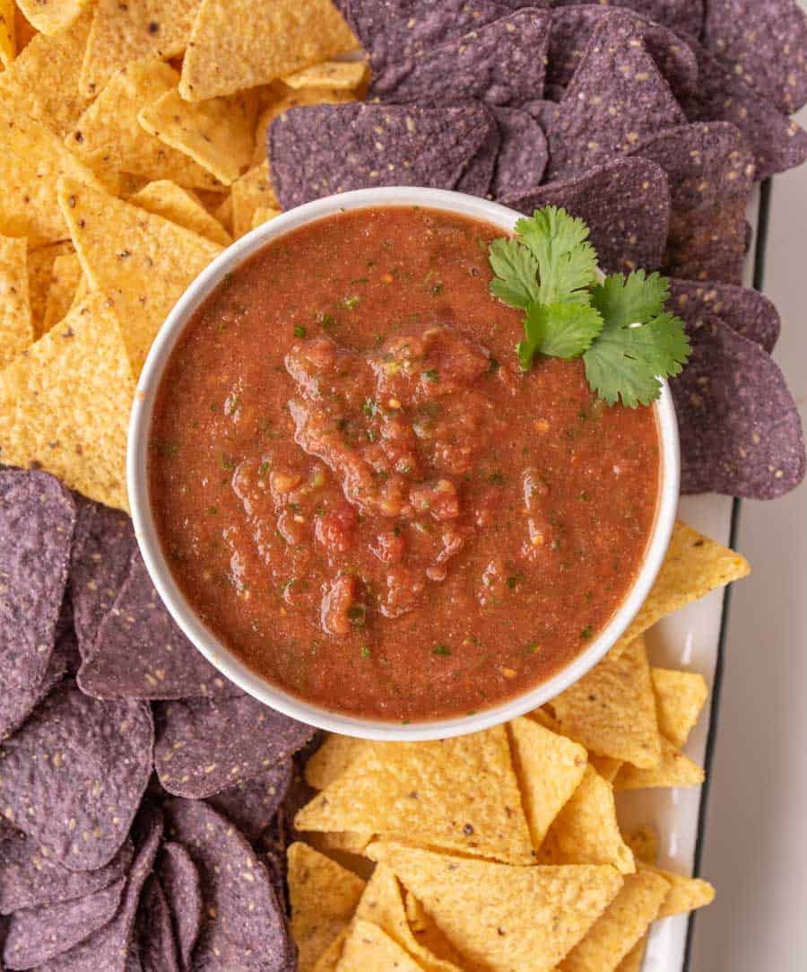 a bowl of blender salsa surrounded by yellow and blue tortilla chips