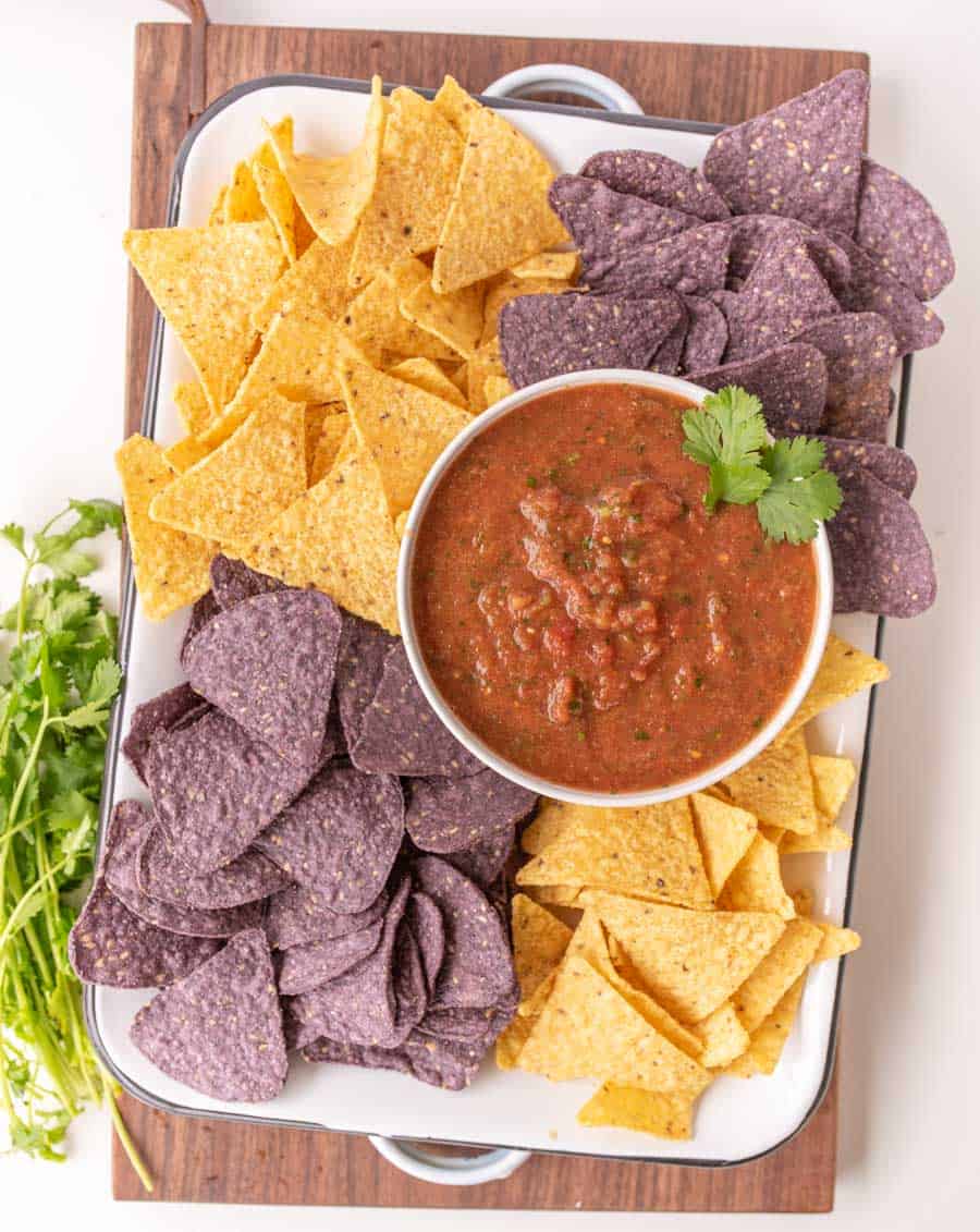 a white tray with a bowl of salsa surrounded by yellow and blue tortilla chips