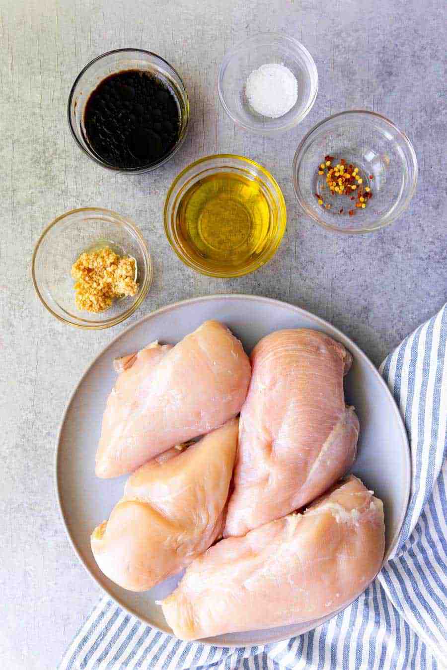top view of a plate of chicken and ingredients for balsamic marinade in bowls next it.