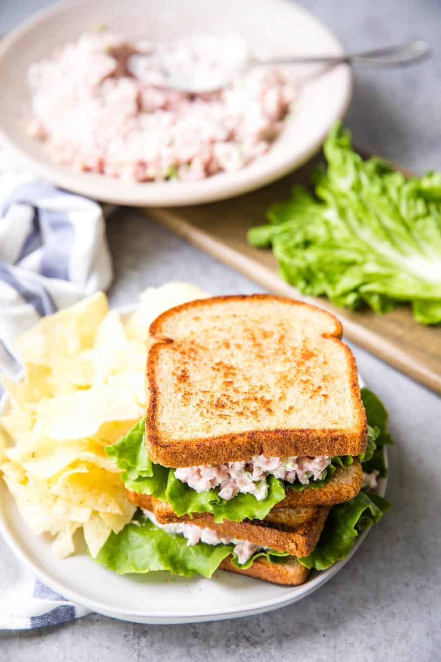 Top view of a ham salad sandwiches stacked on a plate with chips.