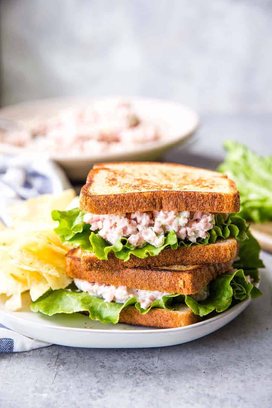 Ham salad sandwiches stacked on a plate with chips.