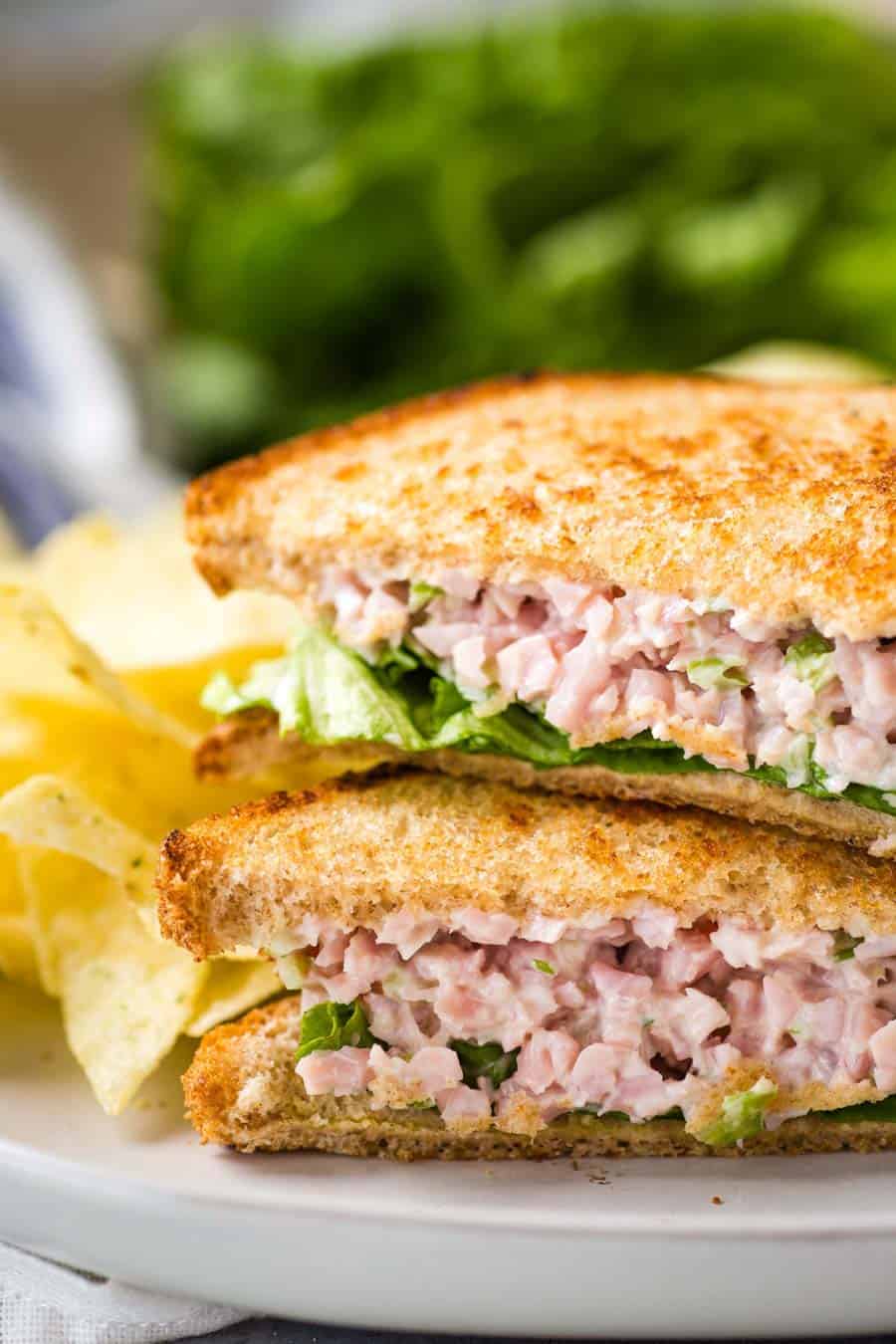 A close up of ham salad sandwiches stacked on a plate with chips.