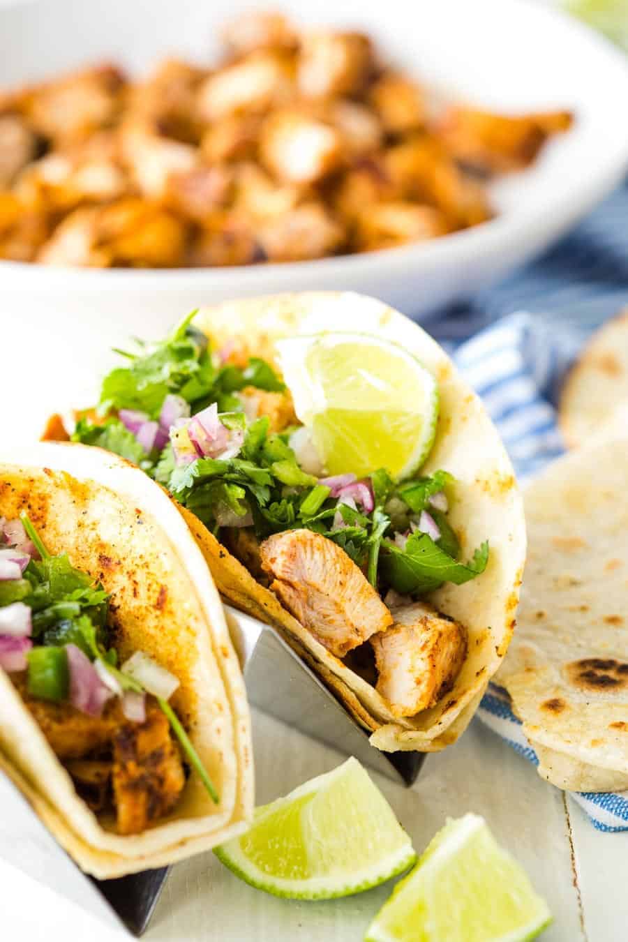 Close up of chicken street tacos topped with cilantro, red onion and limes.