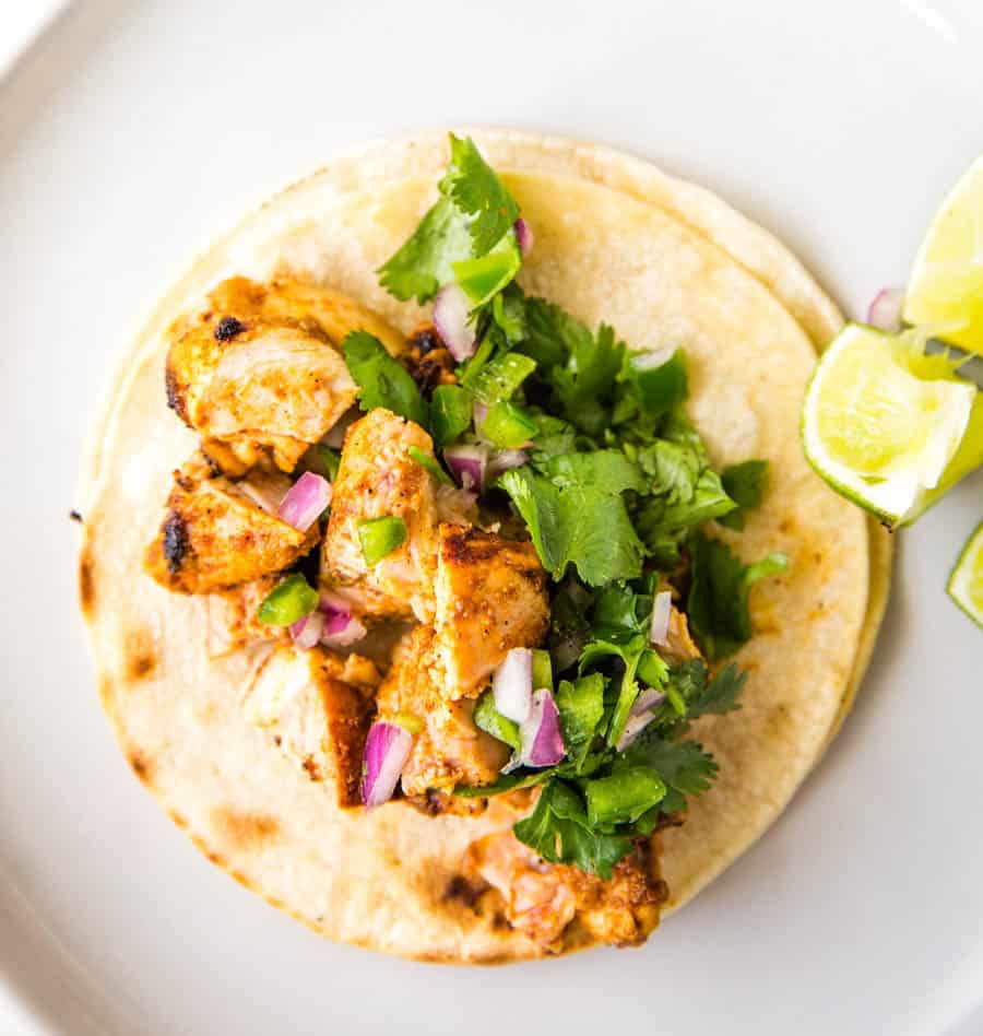 Top view of a chicken street taco laid flat topped with cilantro, red onion, jalapeño and lime.