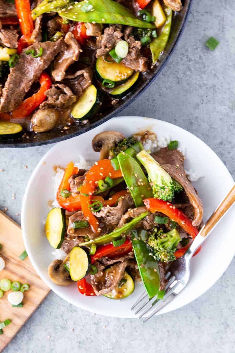 A top view of a white bowl of teriyaki beed and vegetables with the skillet in the background.