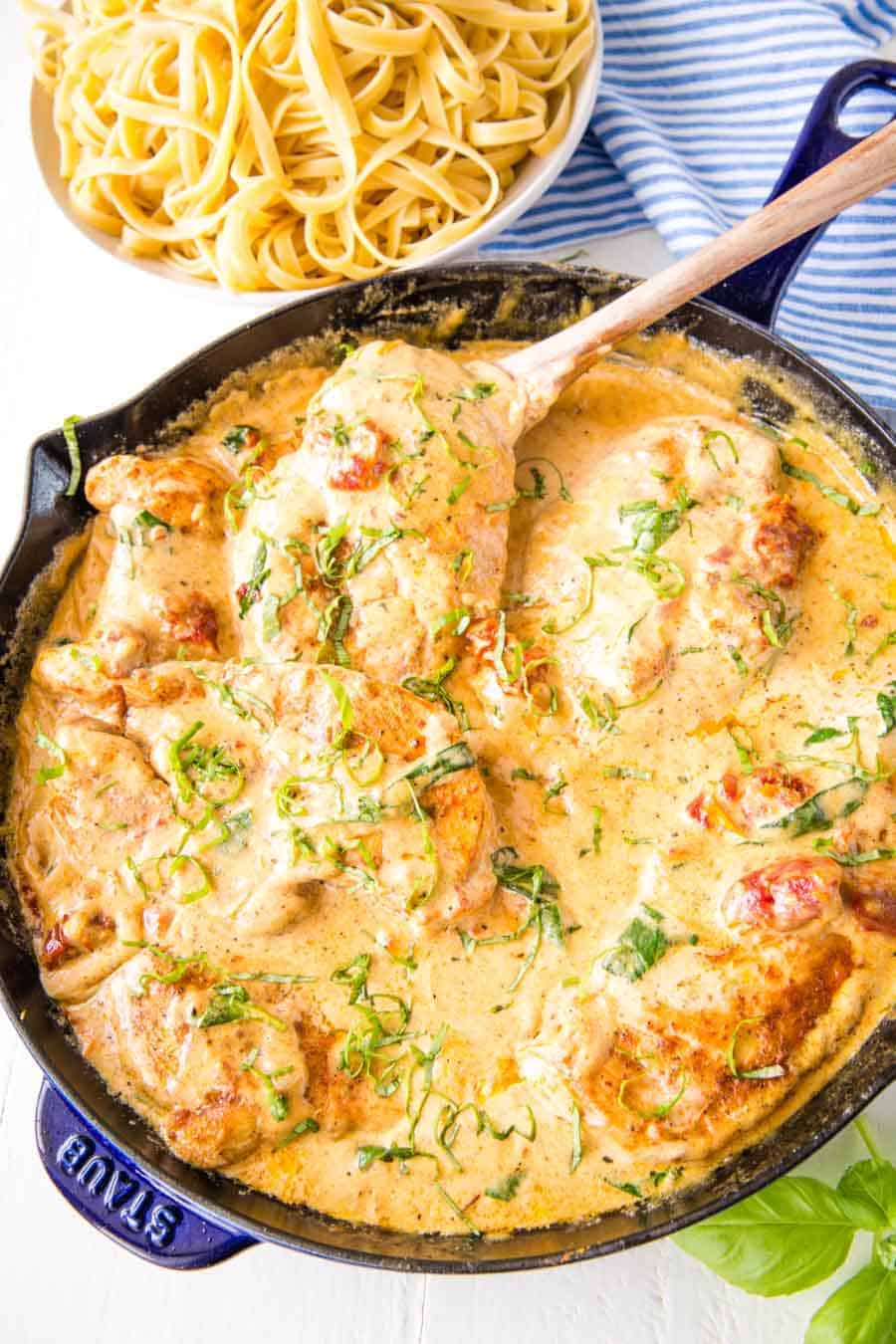 top view of Tuscan chicken in a skillet next to a bowl of pasta.