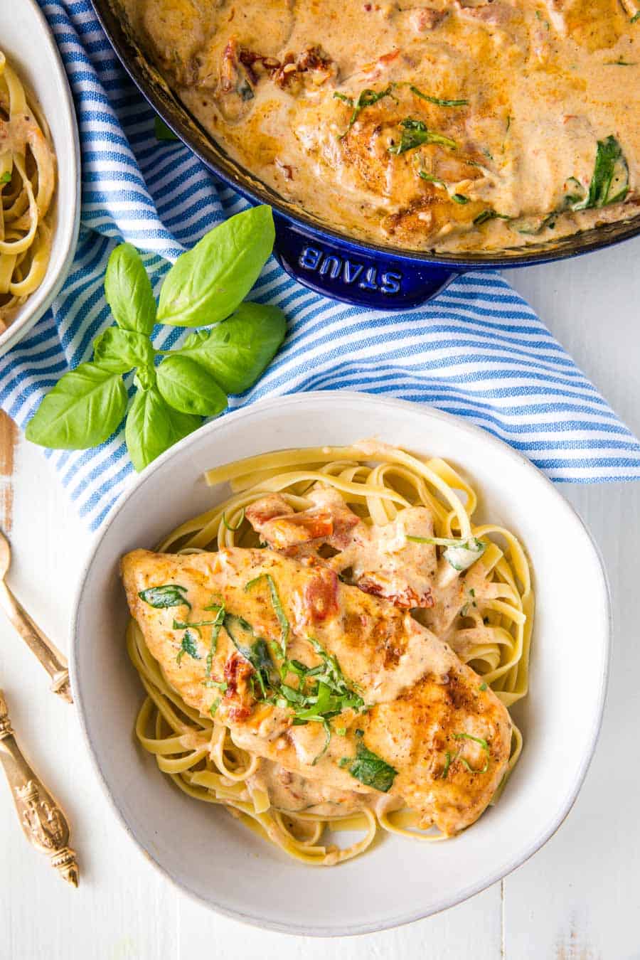 top view of tuscan chicken over pasta next to a cast iron skillet of the tuscan chicken.