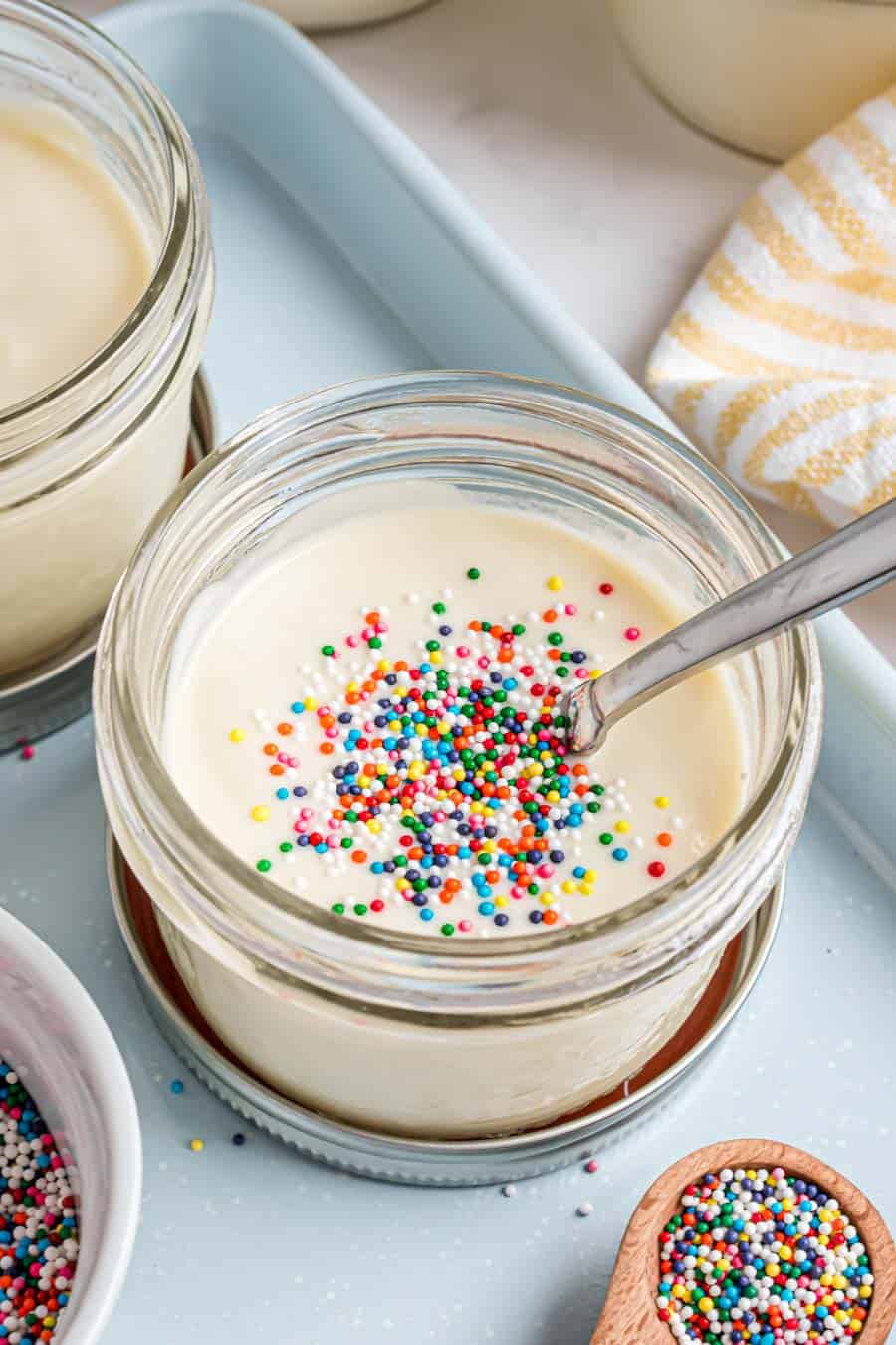 Top view of a jar of vanilla pudding with rainbow sprinkles on top.