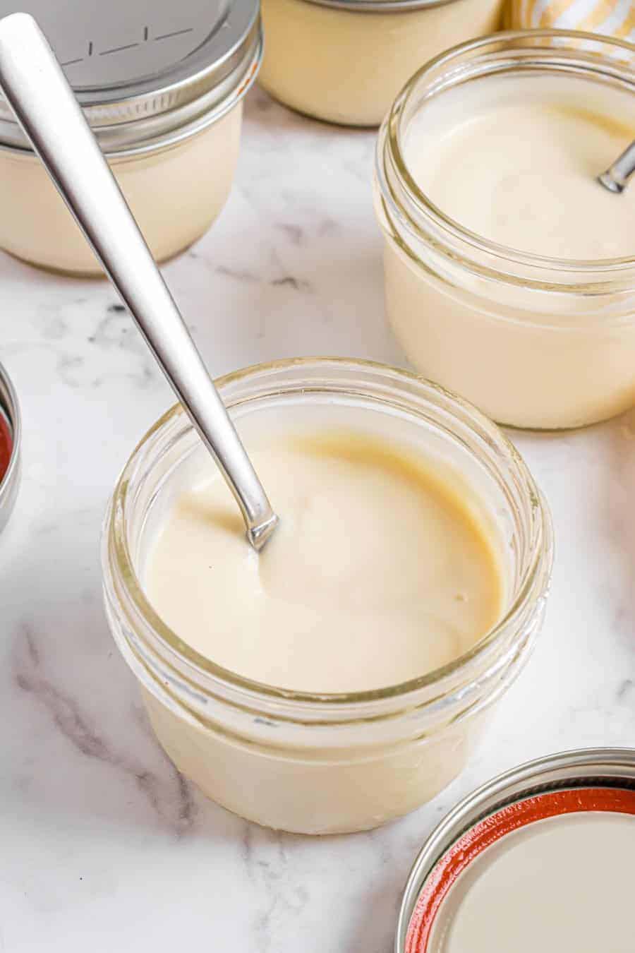 Close up of a jar of homemade vanilla pudding with a spoon in it.