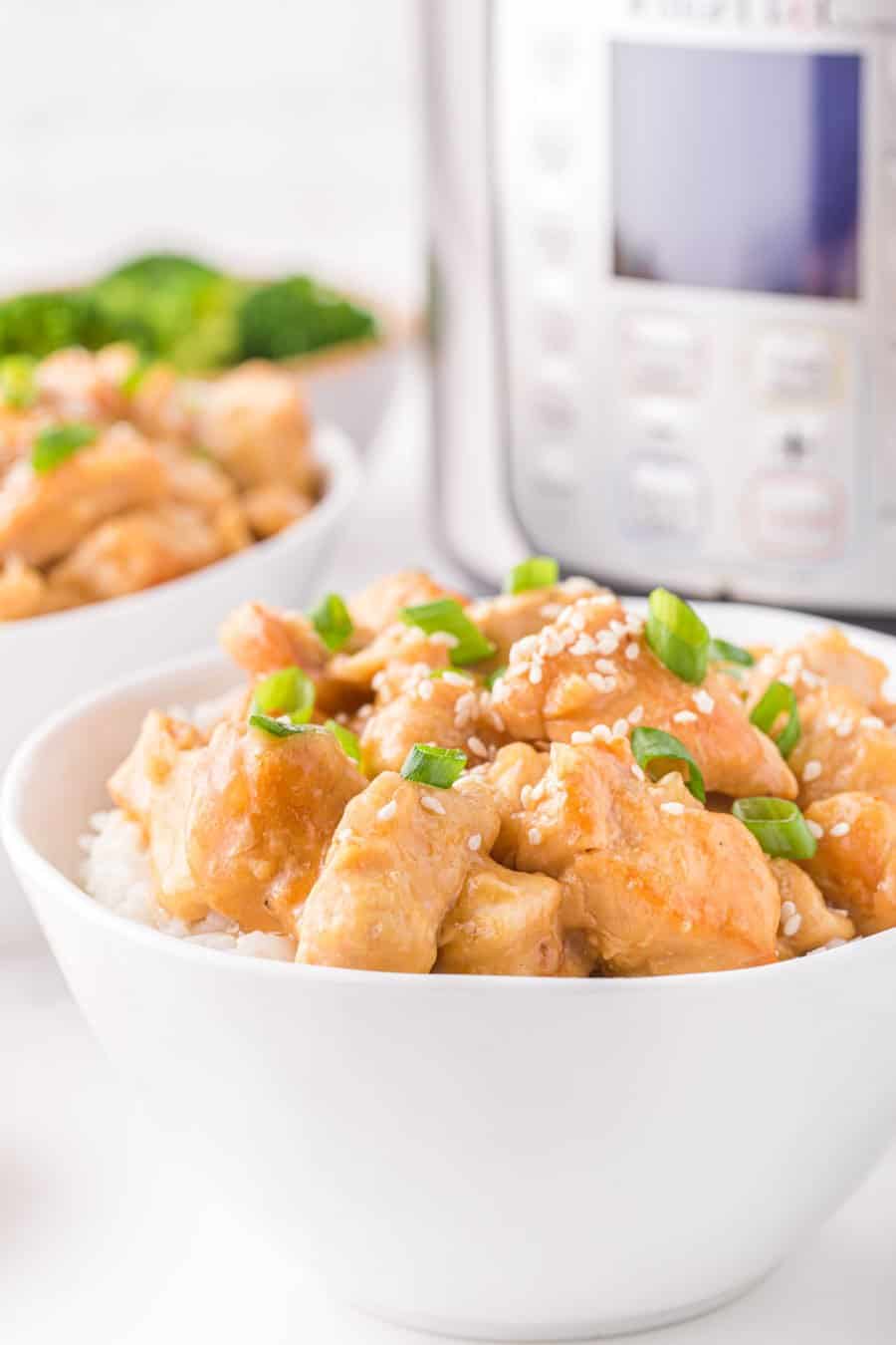 Up close of a white bowl with honey sesame chicken topped with sesame seeds and green onions.