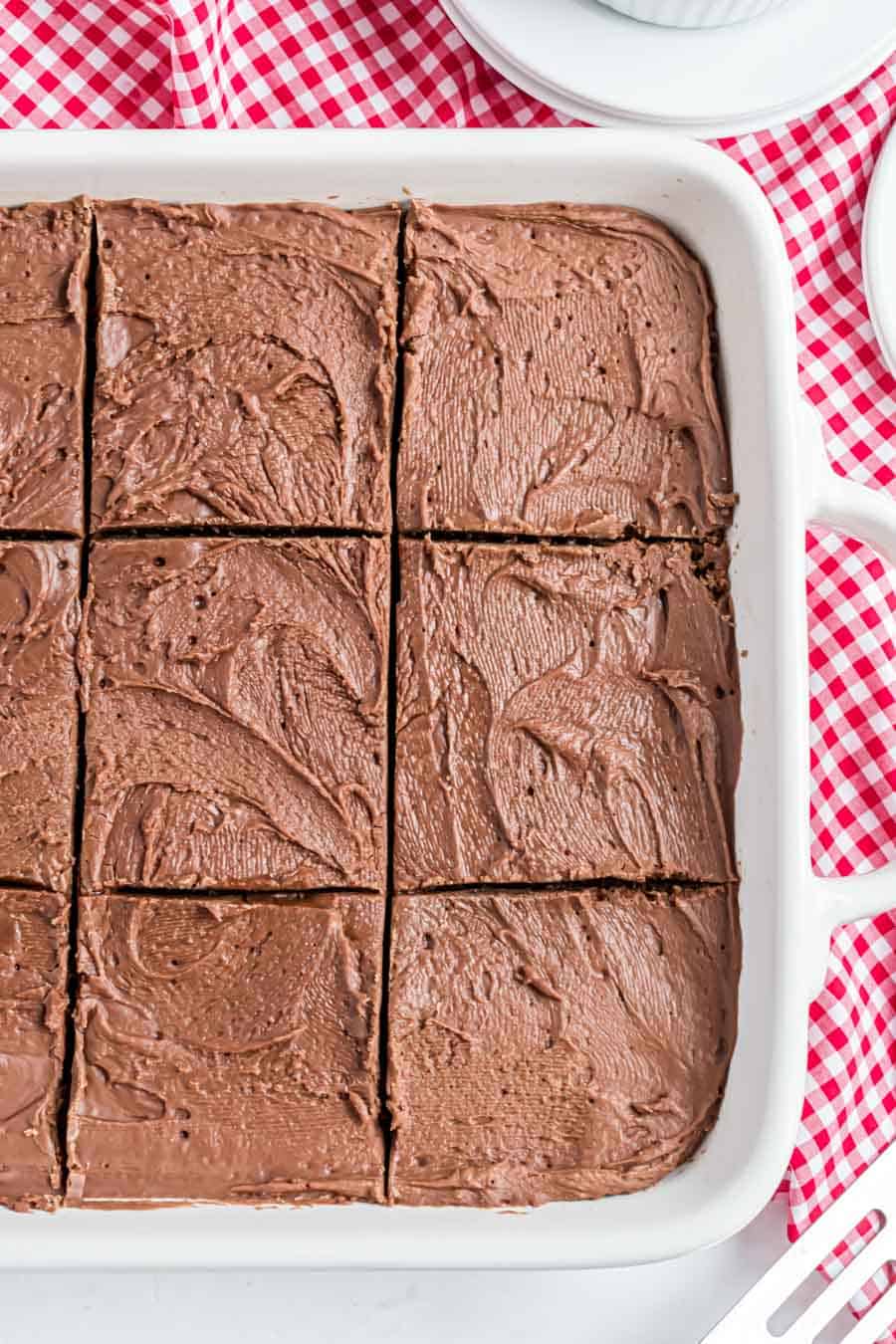 Top view of iced brownies in a white dish on a red and white checkered tablecloth.