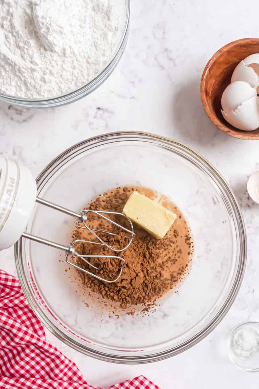top view of ingredients for brownies in a bowl with an electric hand mixer next to it.