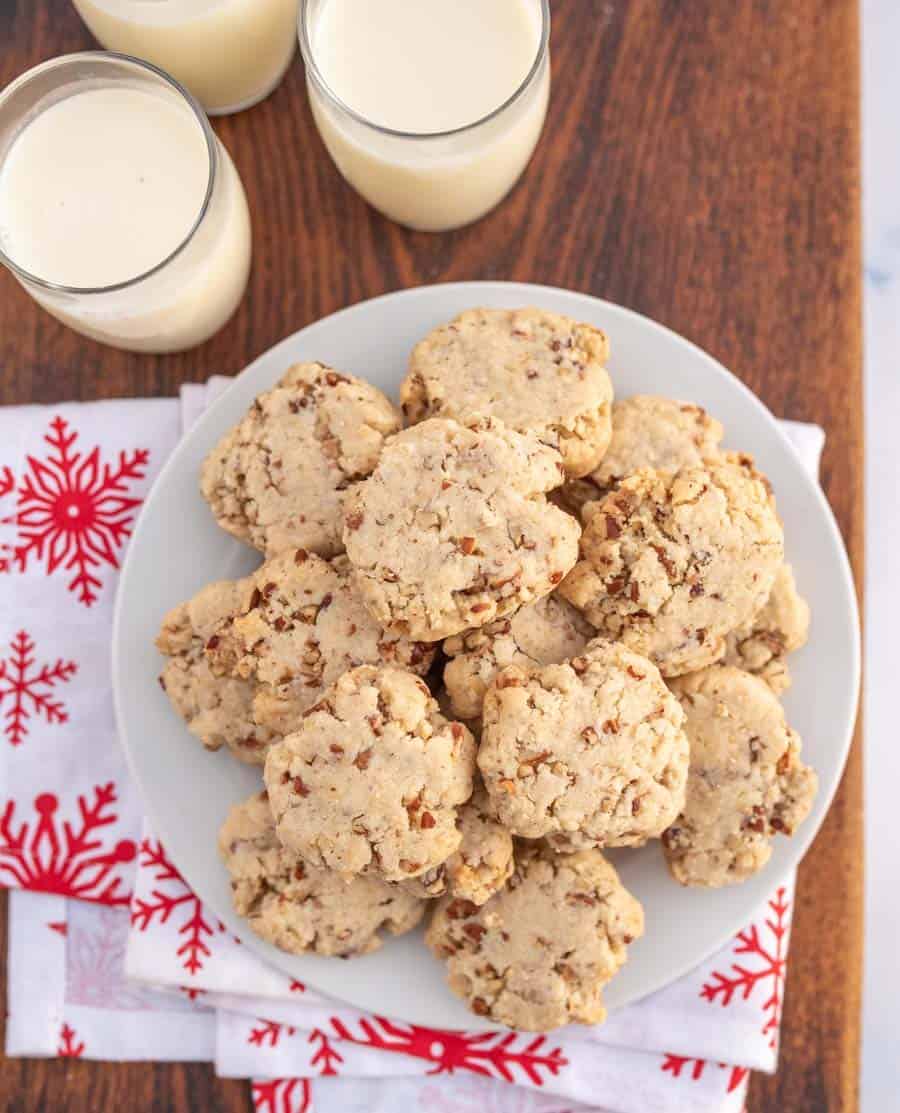 Top view of a plate of pecan sandies on red and white snowflake napkin next to glasses of milk.