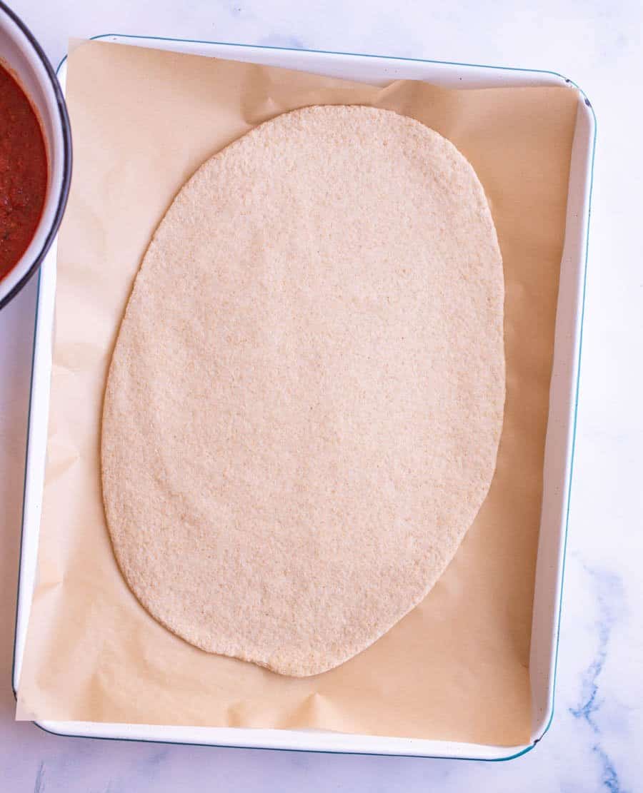 Top view of rolled out wheat pizza dough on parchment paper and a cookie sheet