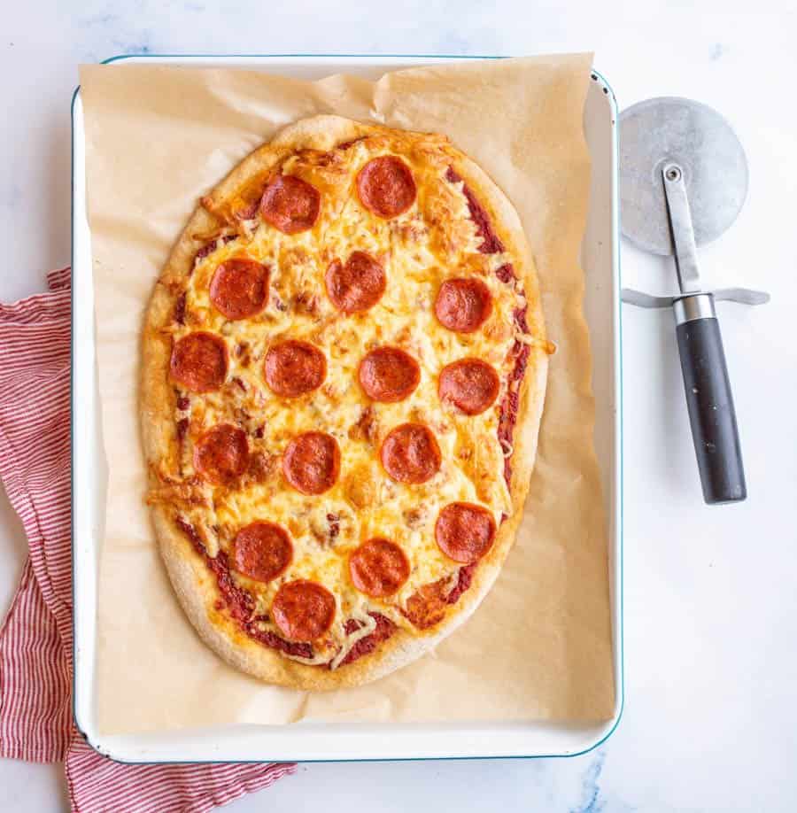 Top view of a perfectly cooked whole wheat pepperoni and cheese pizza with a pizza cutter next to it.