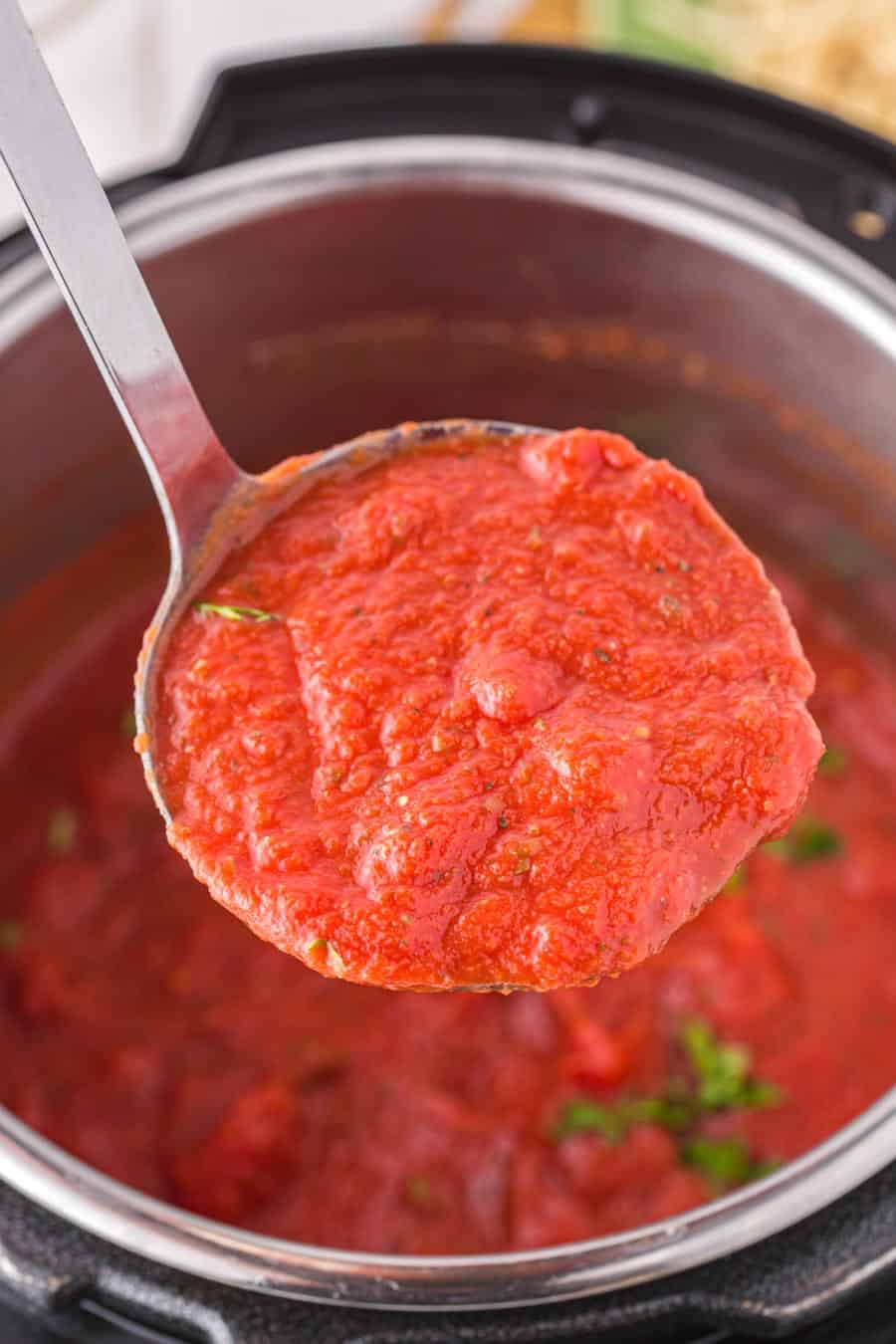 Close up of a ladle full of spaghetti sauce over an Instant Pot.