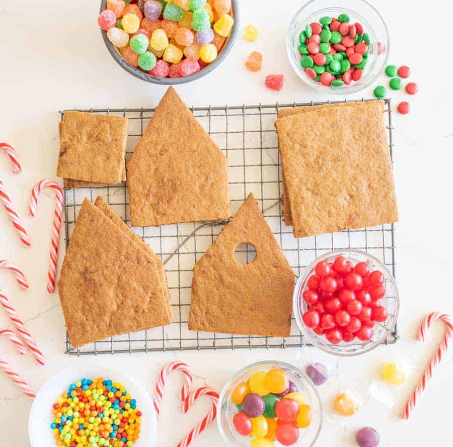Top view of gingerbread house pieces on a drying rack surrounded by bowls of candies.
