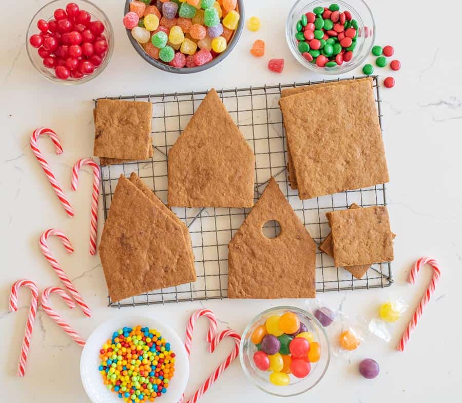 ascetic image of ginger bread house ingredients before construction - cookie pieces in house shape on wire rack and candies all around