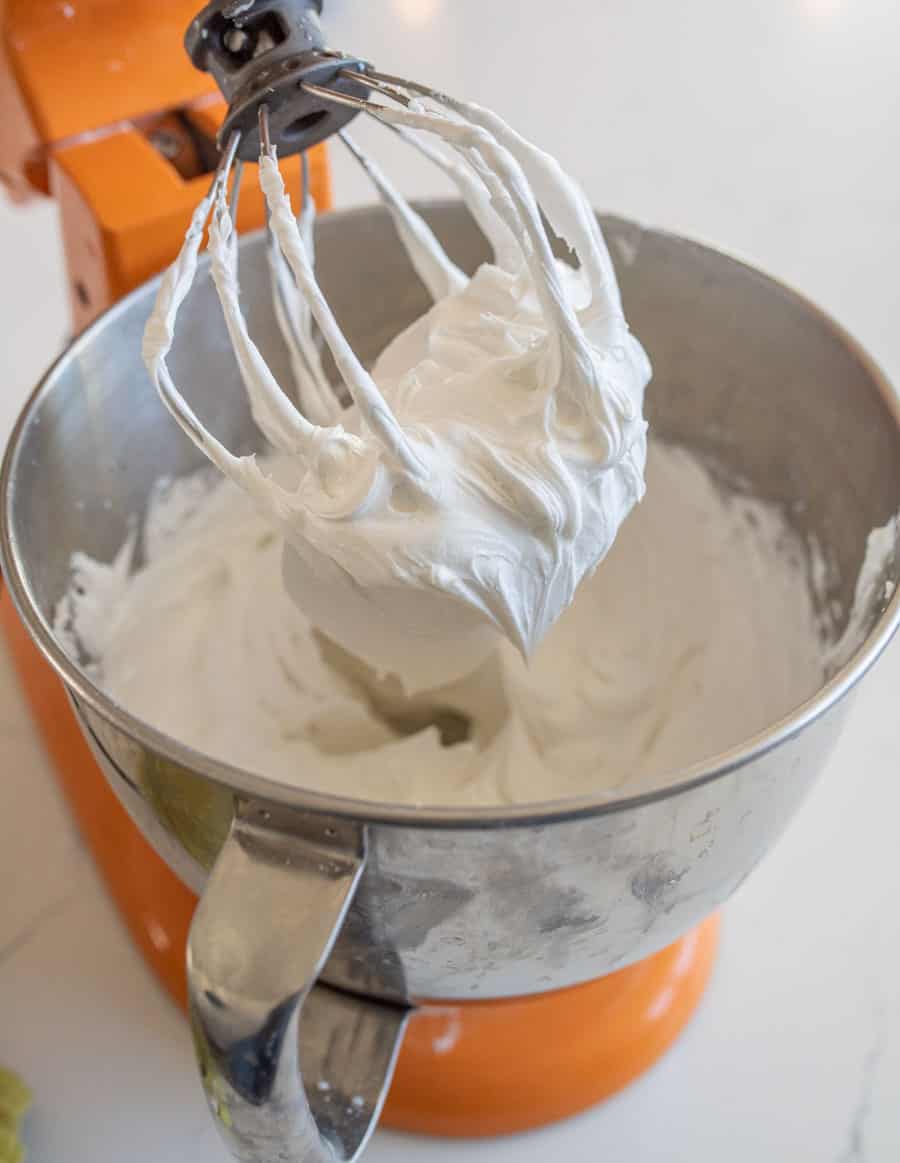 Royal icing in an orange stand up mixer bowl and on the mixing blade.