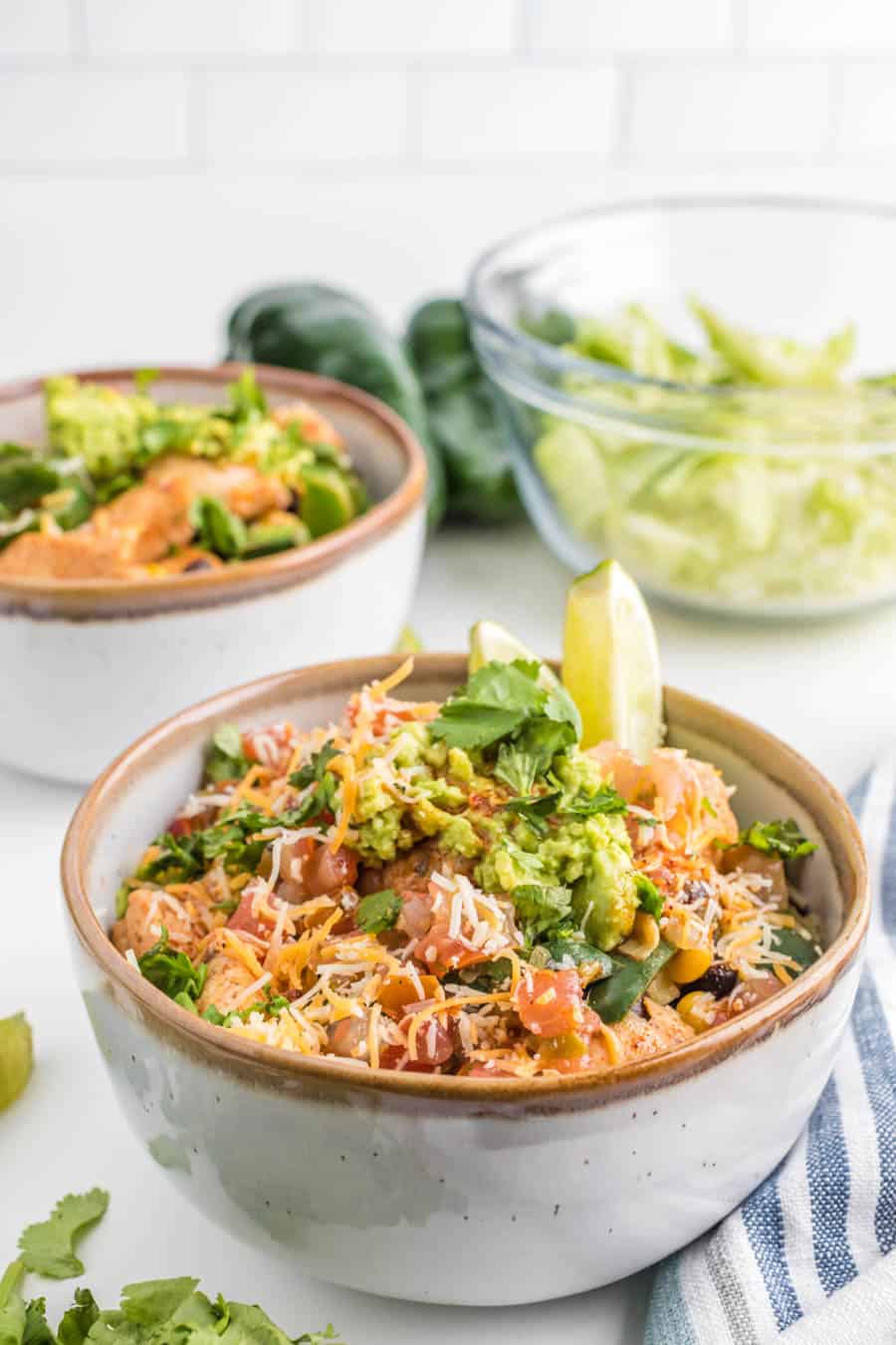 Close up of a chicken burrito bowl with lettuce, tomatoes, cheese, guacamole, cilantro, and limes.