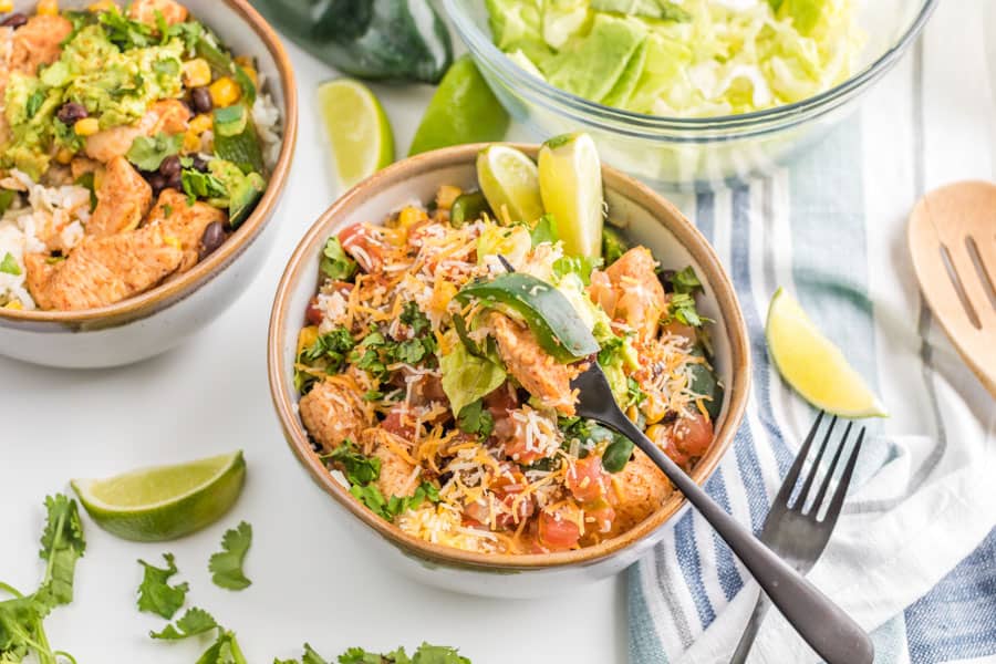 Two burrito bowls packed with chicken, lettuce, pico de Gallo, avocados, and limes.