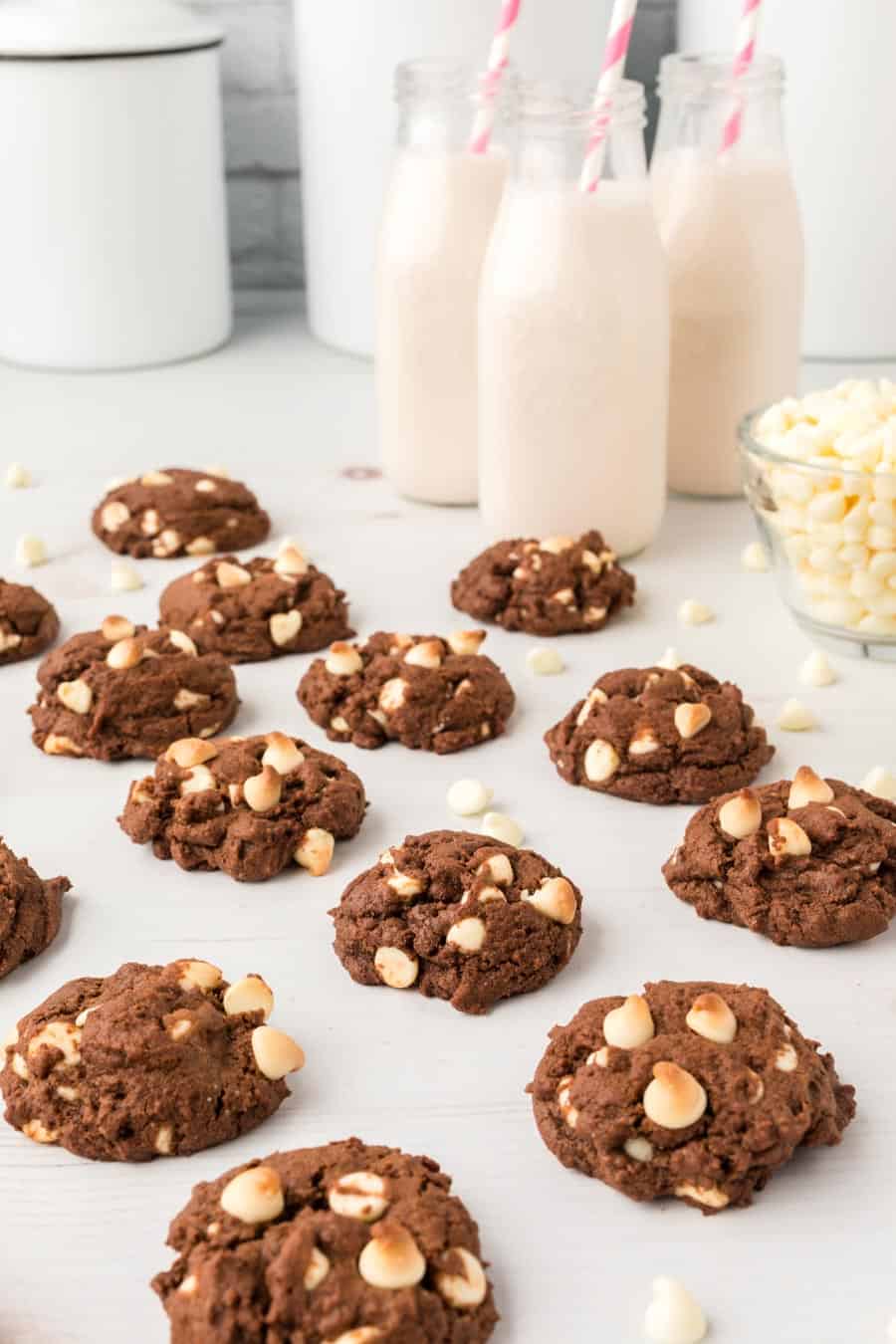 chocolate cookies with white chips on the table with milk in the background.