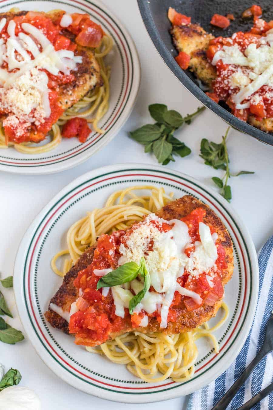 Top view of white plates with red and green stripes around the edge with chicken, topped with a red sauce and white shredded cheese on them.