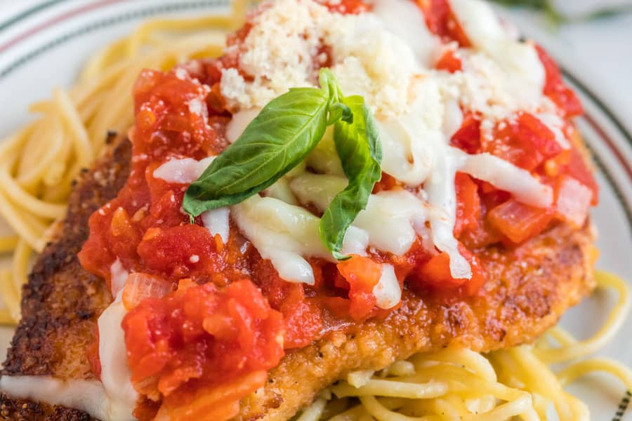 Close up picture of breaded chicken topped with red sauce and mozzarella cheese on a bed of spaghetti noodles.