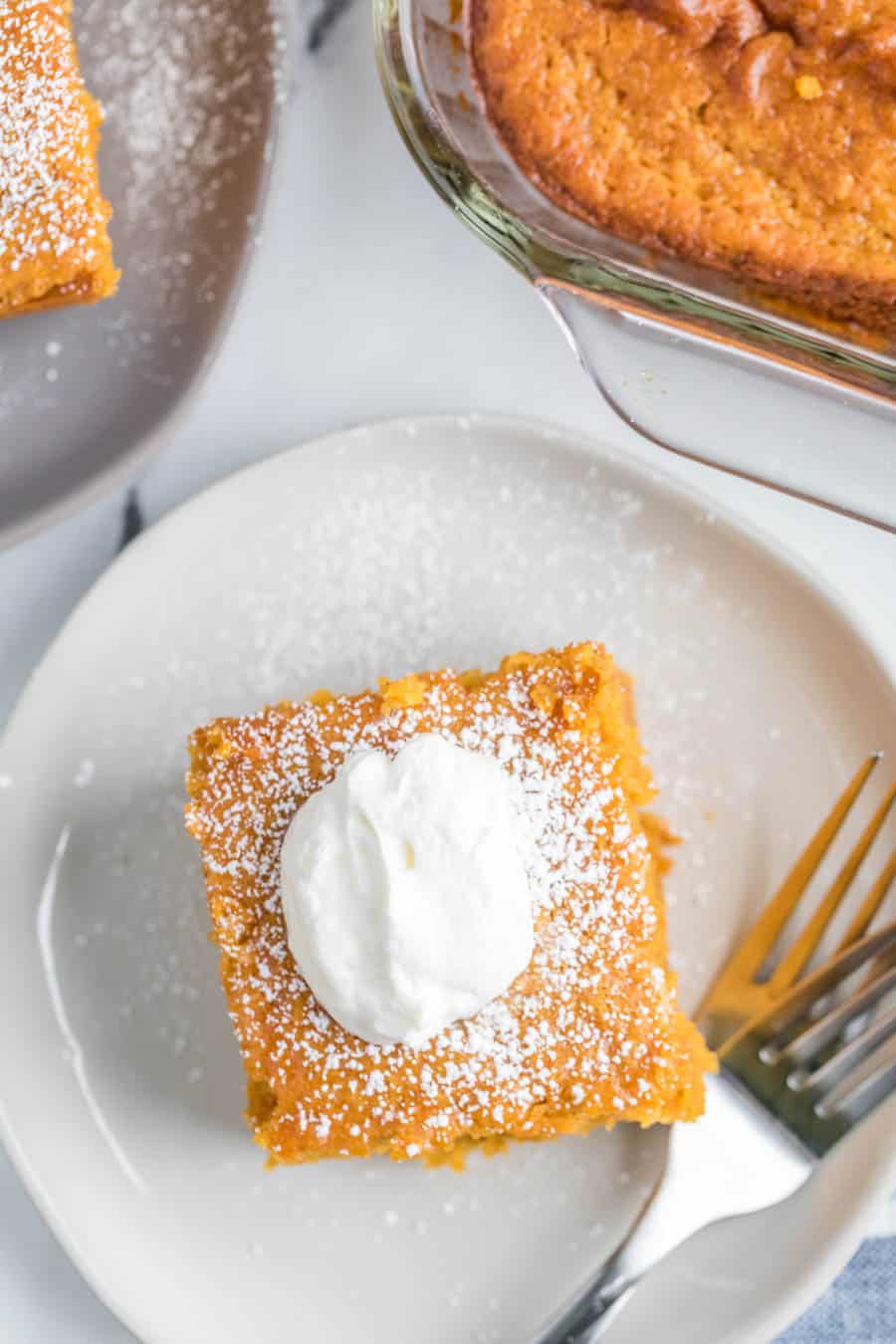 Top view close up of a square serving of extra thick pumpkin cake on a white plate with a dollop of whipped cream.