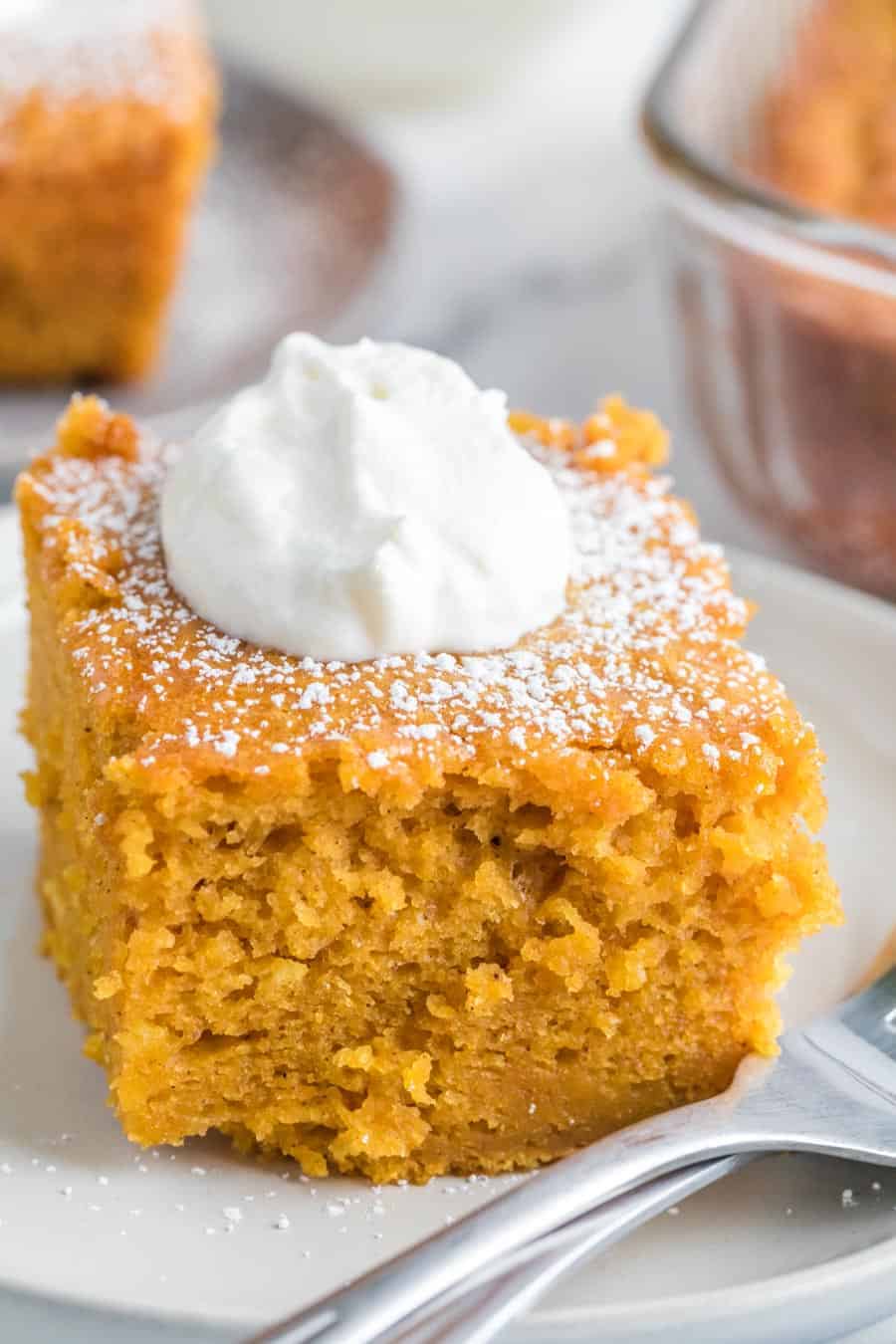 Close up - side view square servings of extra thick pumpkin cake on a white plate with a dollop of whipped cream.