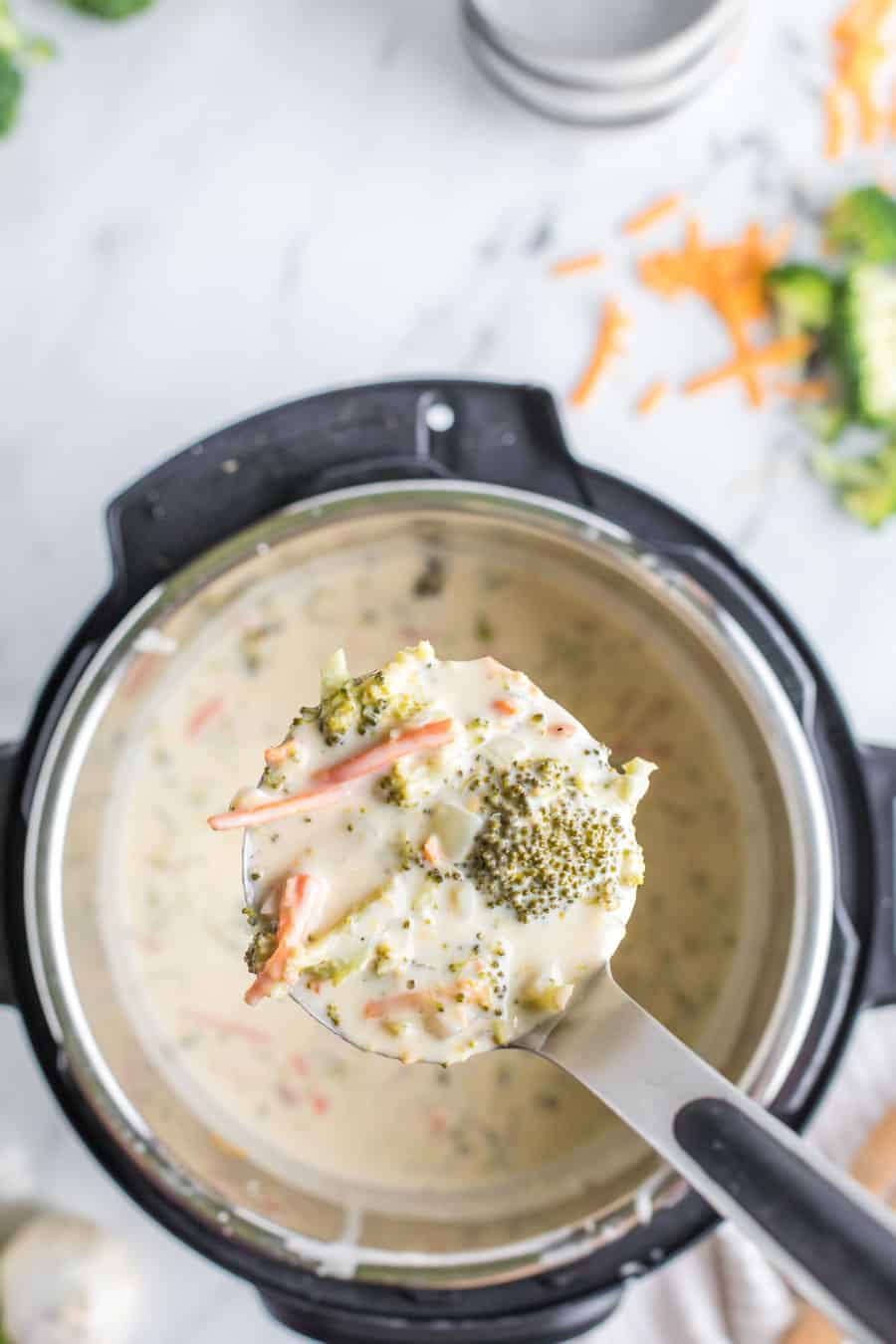 A ladle filled with broccoli and cheese soup above an instant pot filled with the soup.