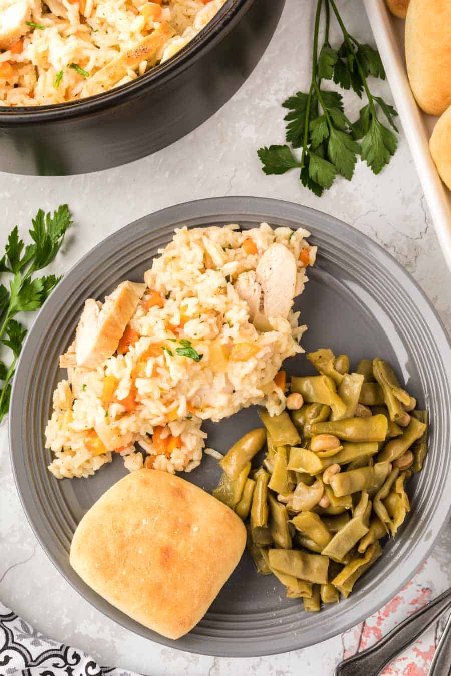 Top view of a plate with chicken and rice mixture, a roll, and green beans.