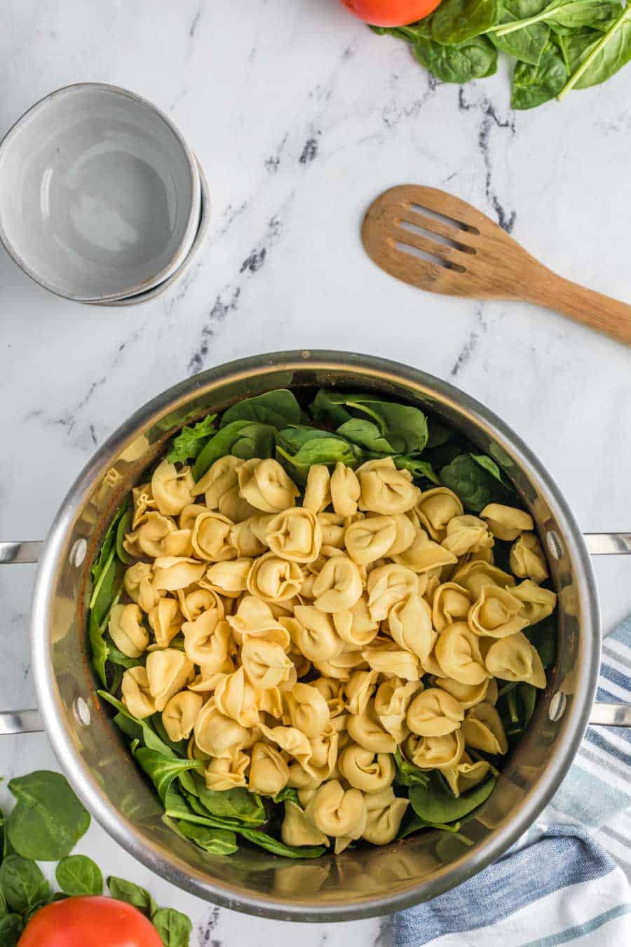 Top view pot with tortellini laid over a bunch of spinach.