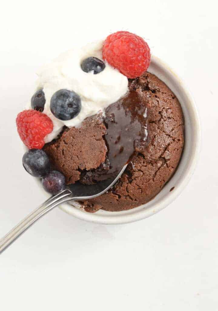 Top view of a chocolate molten lava cake with a spoon through the center and berries and whip cream on one side.