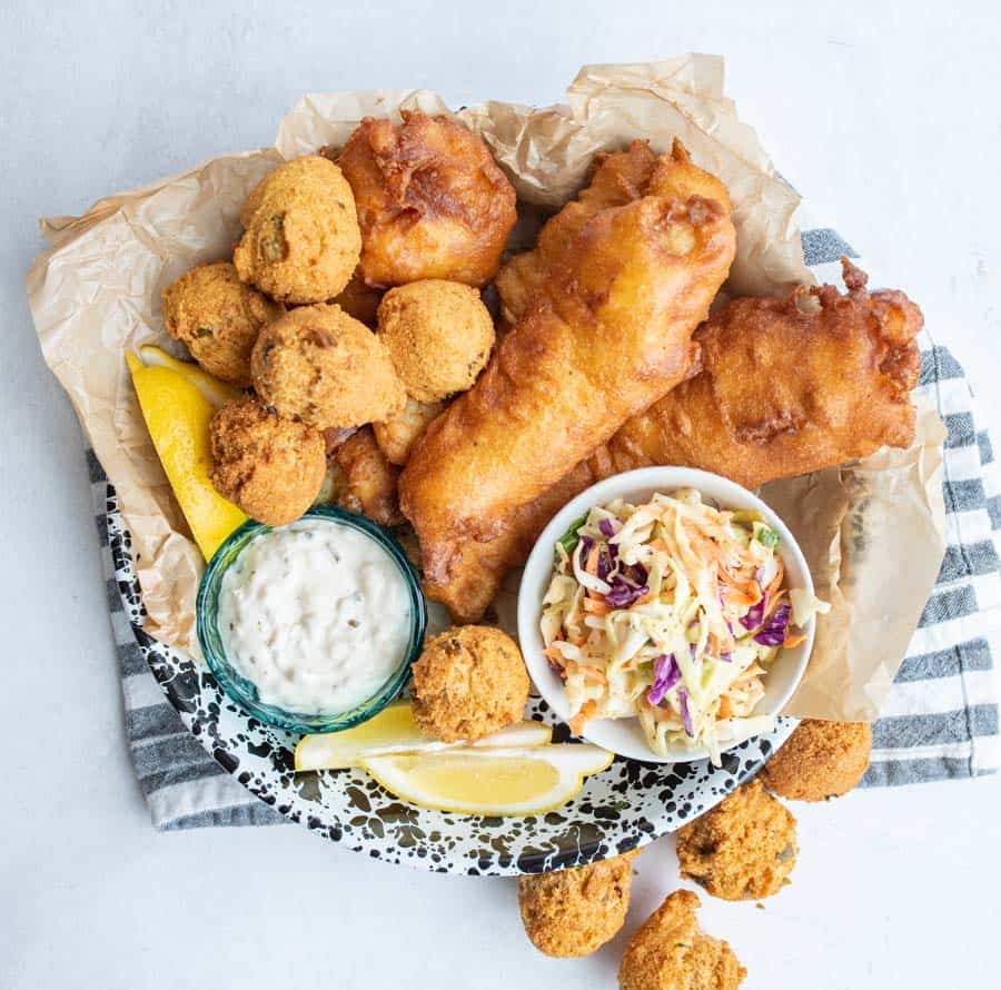 crispy deep fried and beer battered fish and hush puppies with tartan and lemons and coleslaw.