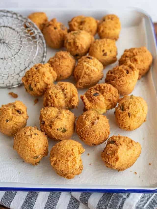 close up of round balls of hush puppies fresh out of the fryer on a baking dish.