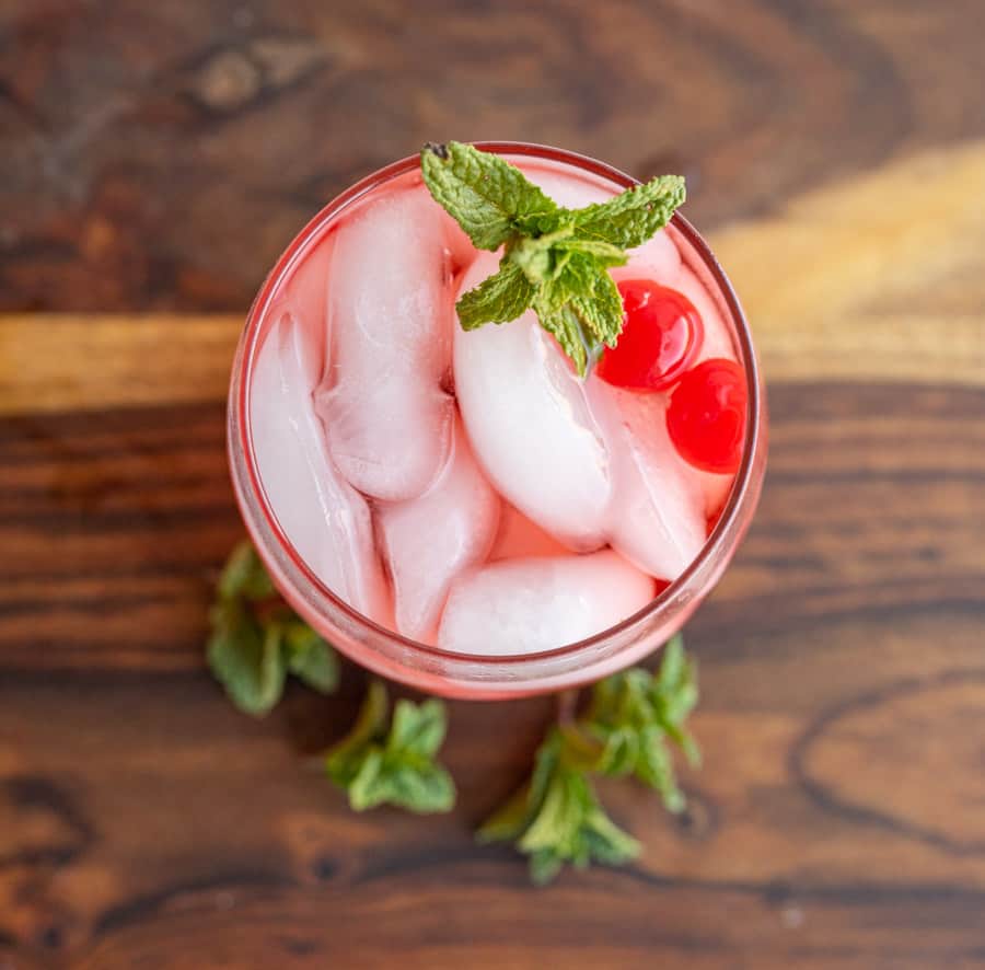 top view tumbler of a red "Shirley-Temple" drink with ice cherries and garnish.