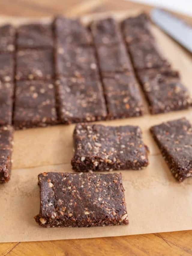 Several rectangular chocolate energy bars with visible nut pieces are arranged on parchment paper, some separated in the foreground and others grouped in the background. A knife is partially visible in the corner.