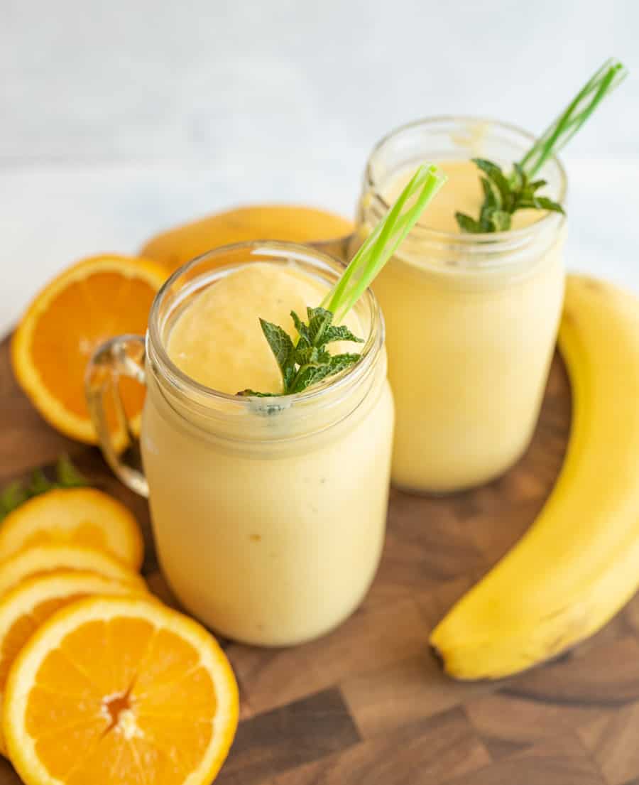 two tropical yellow smoothies in mason jars with a handle.