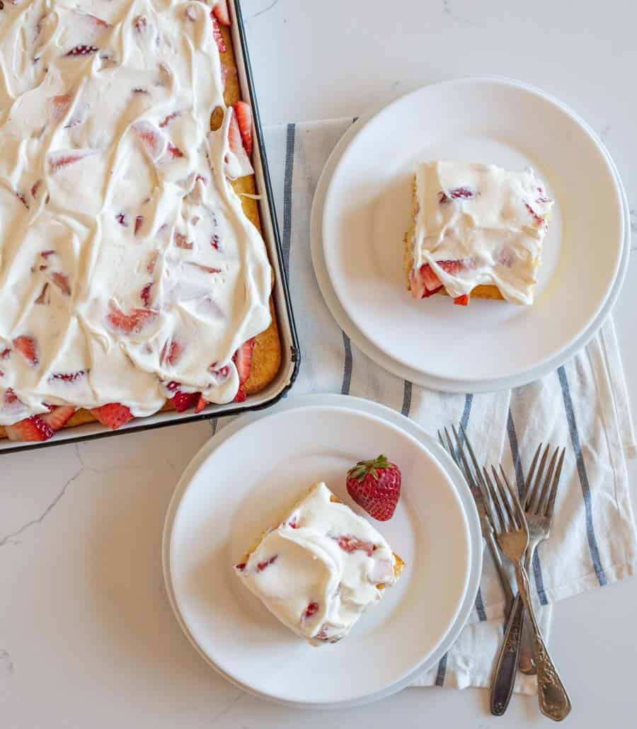 top view of a sheet pan strawberry shortcake and two servings dished onto white plates.