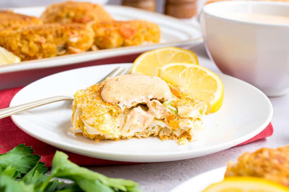 Beautiful plated crabcake with lemons on the side on a white plate.
