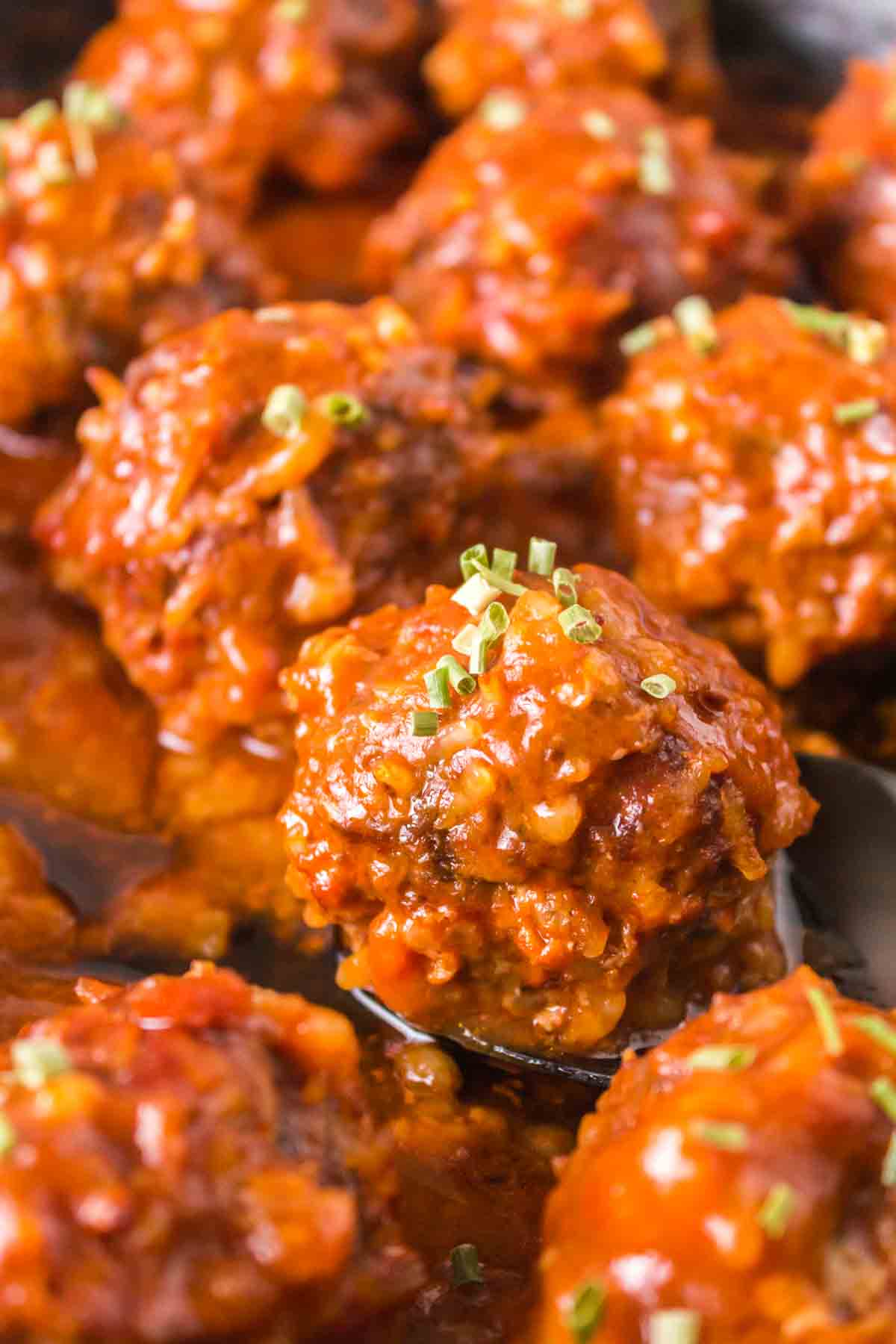 Close-up of several porcupine meatballs covered in a rich, red tomato sauce and garnished with finely chopped herbs, arranged closely together on a serving dish.