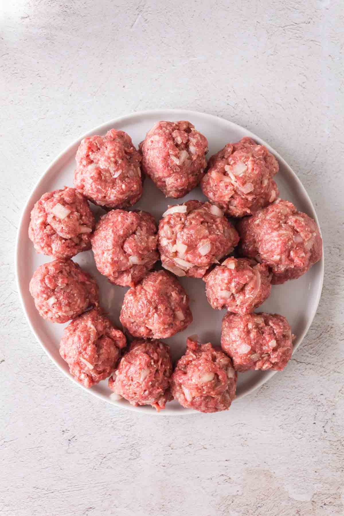 A white plate filled with raw porcupine meatballs mixed with chopped onions, set on a light-colored surface.