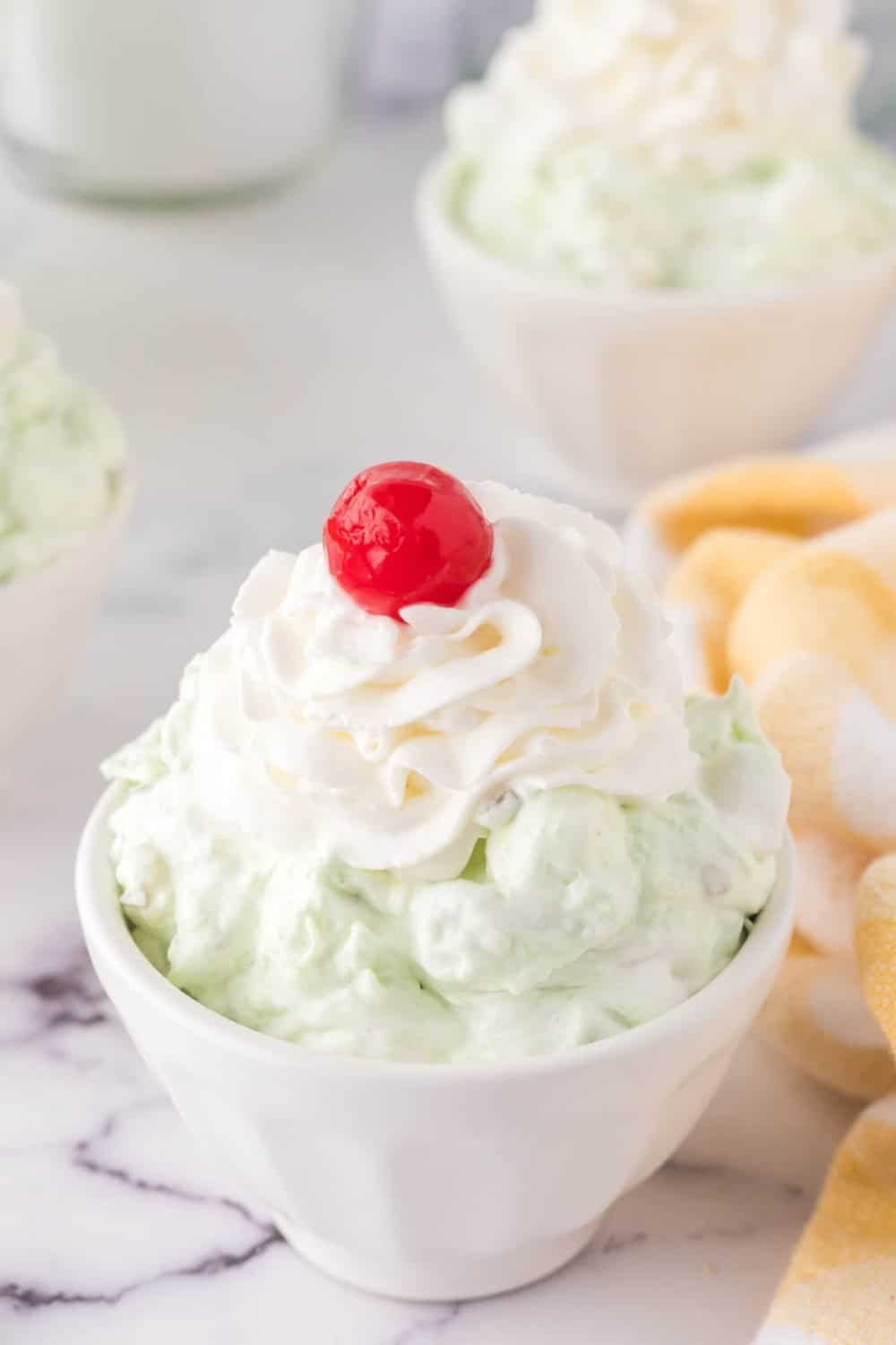 Pistachio jello salad topped with whipped cream and a cherry.