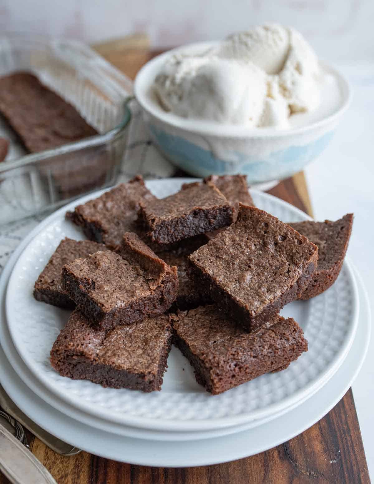square fudge brownies on a plate with a bowl of ice cream to the side