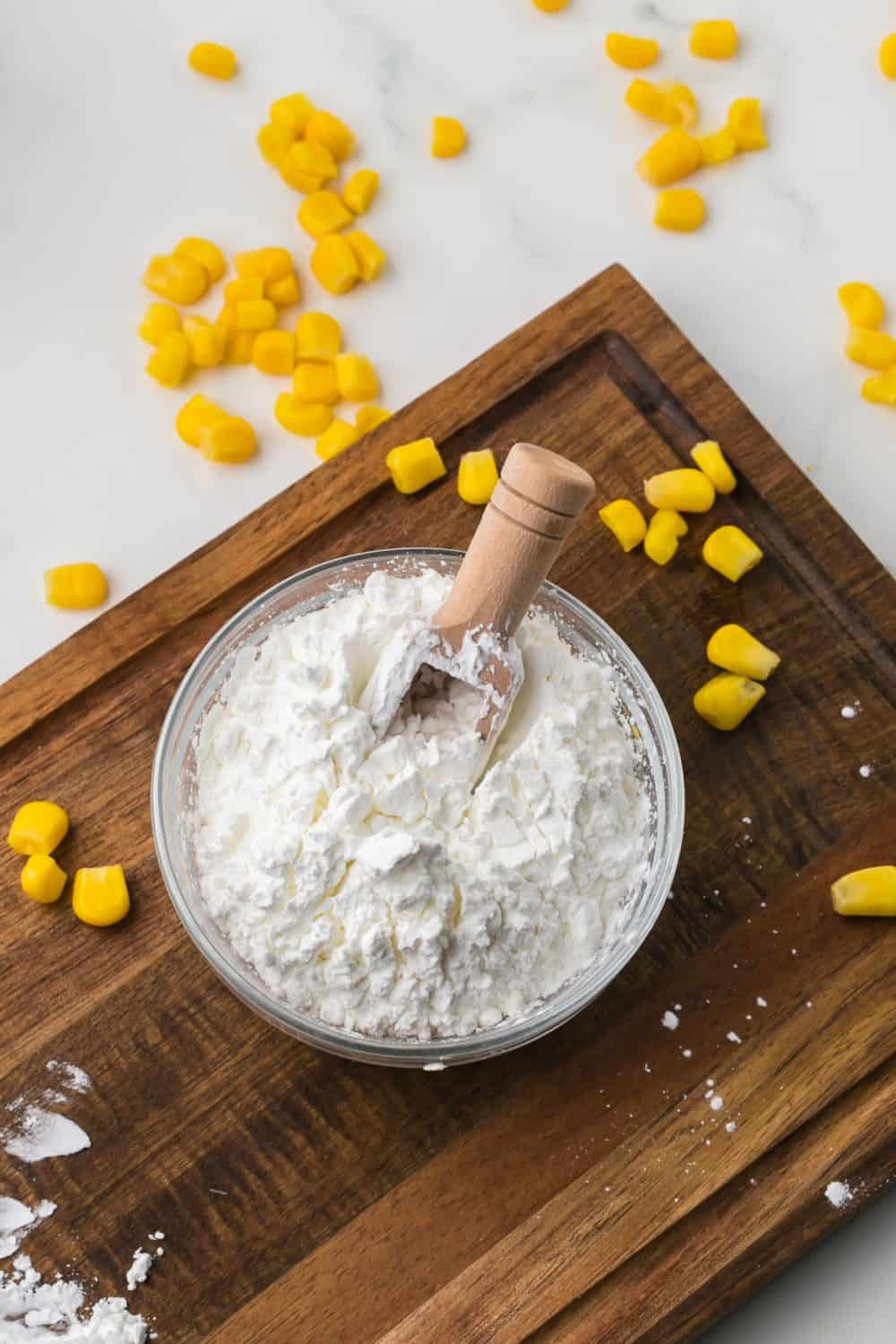wooden cutting board with kernels of yellow corn glass bowl with white starch.