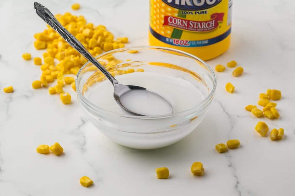 glass bowl with water and Corn starch yellow corn and a metal spoon.