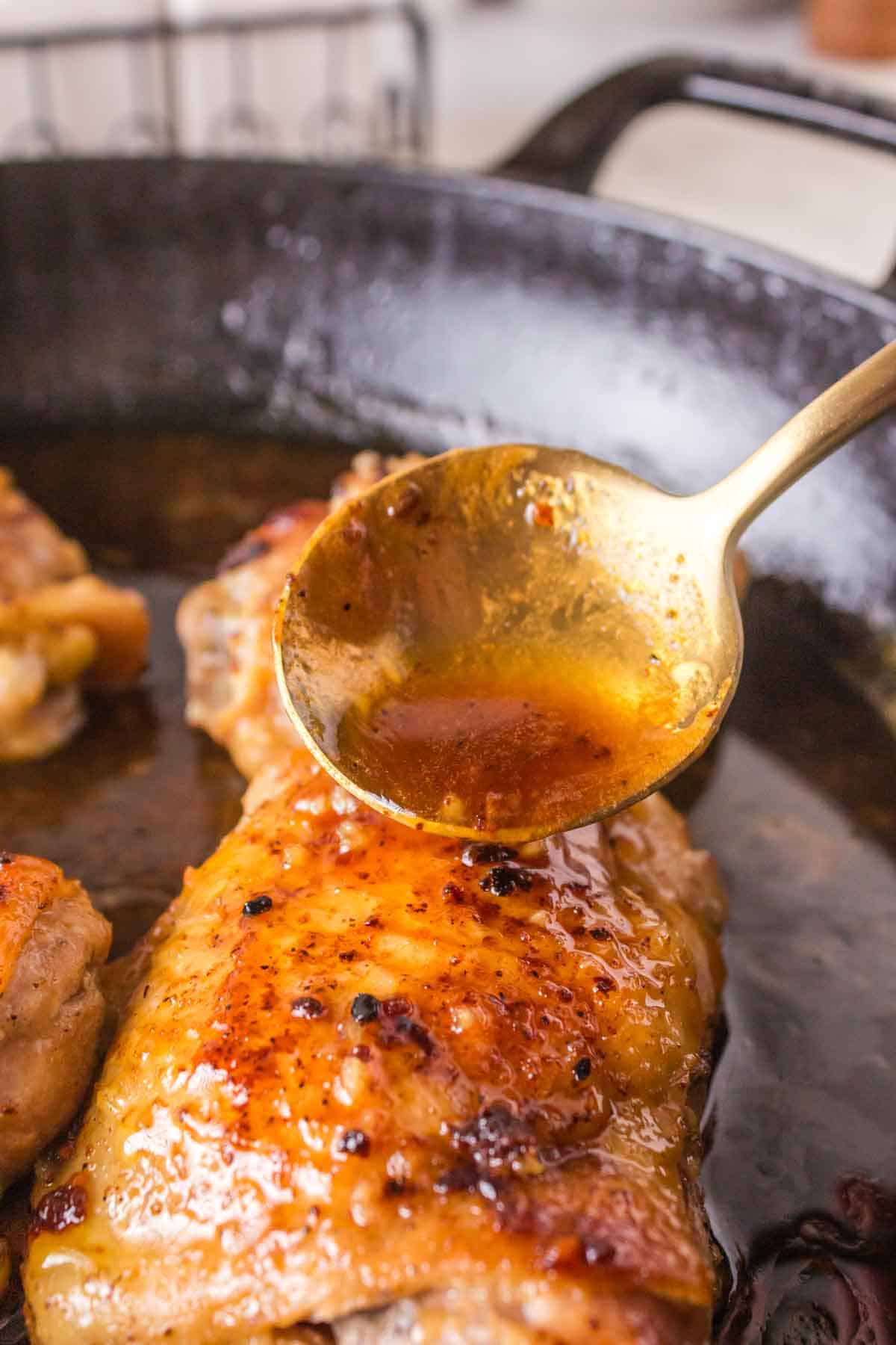seared chicken thigh in a cast iron pan with honey garlic sauce on a spoon